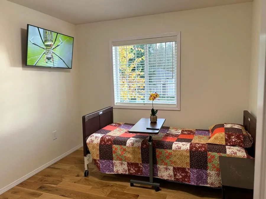 A resident's bedroom with a patchwork quilt, an over-bed table with fresh flowers and a window