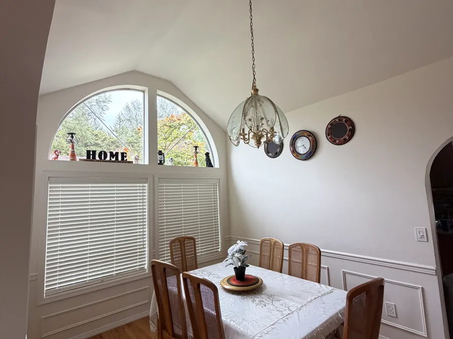 The dining room with a laid table for six under a tall arched window