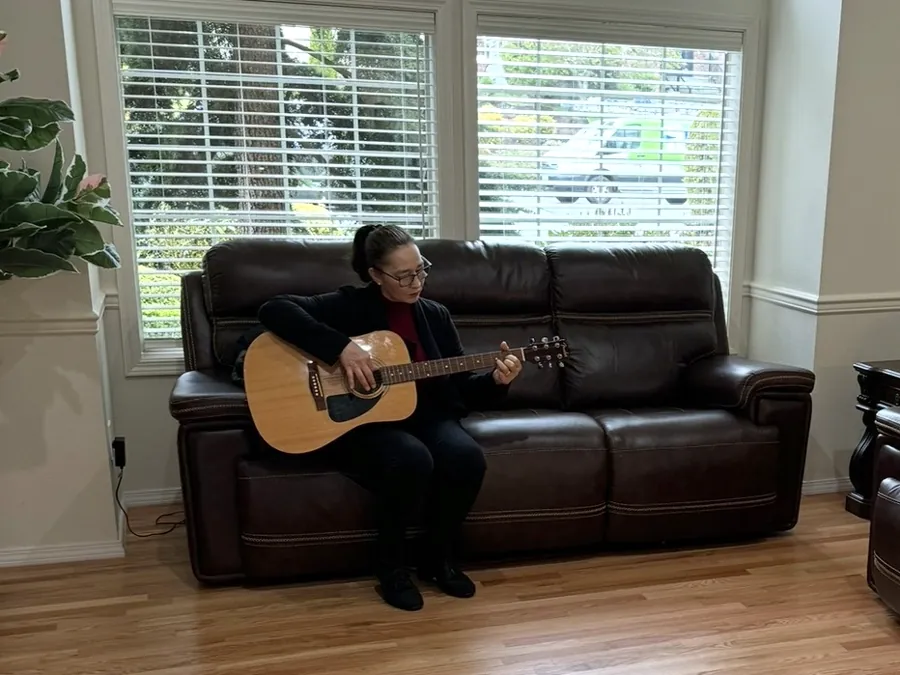 Somebody playing an acoustic guitar on the sofa in the living room
